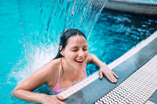 Close-up da mulher sorridente sob fluxo de água na piscina.