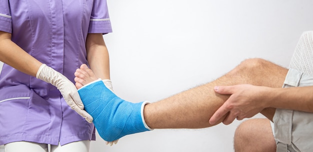 Close-up da perna de um homem engessada e uma tala azul após enfaixamento em um hospital.
