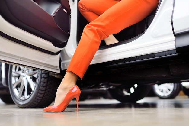 Close-up da perna de uma mulher em um terno vermelho e sapatos vermelhos no contexto de um carro. o conceito de uma mulher dirigindo um carro.