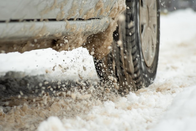 Close-up da roda do carro dirigindo na neve derretida Lama de degelo de inverno na estação fria da estrada