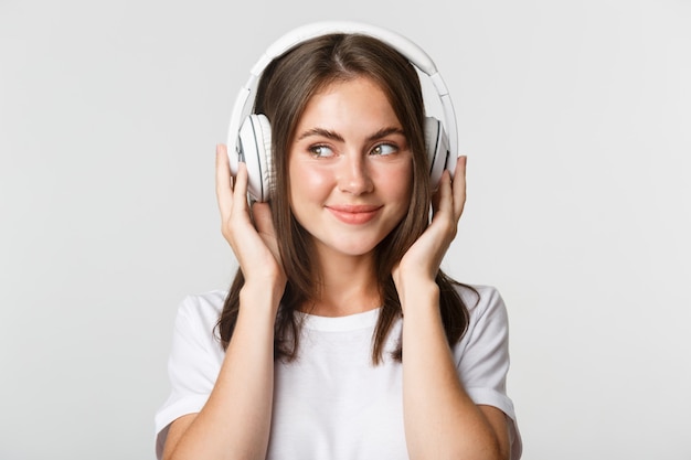 Close-up da sorridente menina morena atraente ouvindo música em fones de ouvido, desfrutando de um podcast interessante.