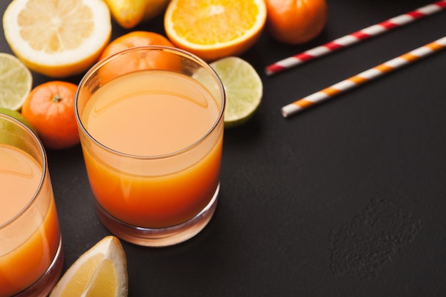 Close up da variedade de cítricos e copo de suco de laranja em fundo preto. Desintoxicação, café da manhã e conceito de estilo de vida saudável, copie o espaço