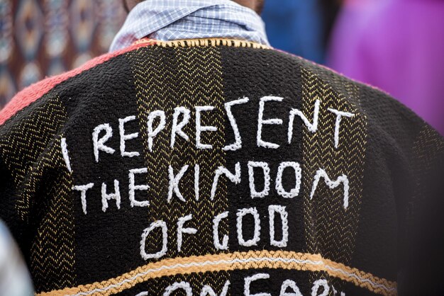 Close-up das costas de uma pessoa vestindo um casaco com "Eu represento o reino de Deus" costurado nele