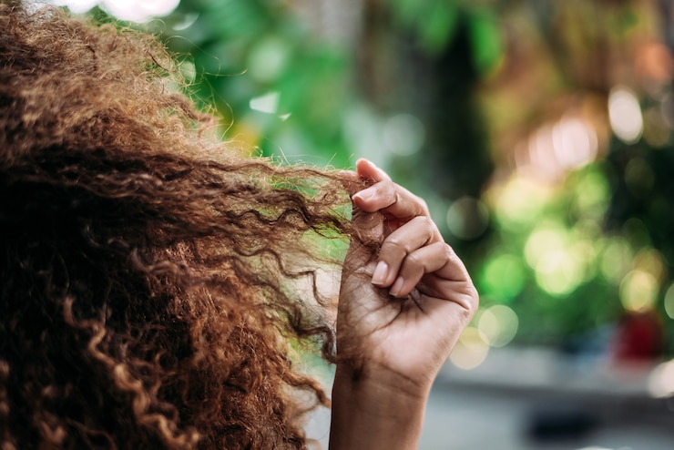 Foto close up das mãos da mulher que tocam em seu cabelo encaracolado.