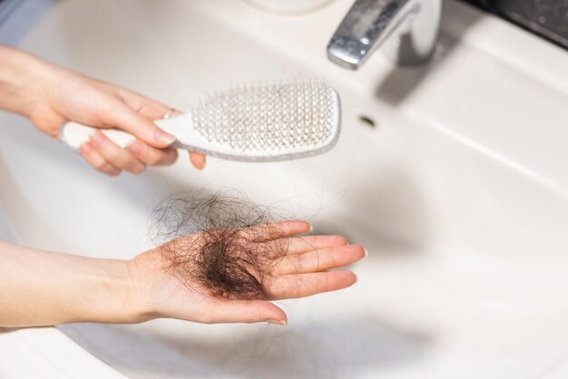 Foto close-up das mãos da mulher segurando o pente sobre a pia e mostra um grande monte de cabelo perdido na palma conceito de calvície e alopecia