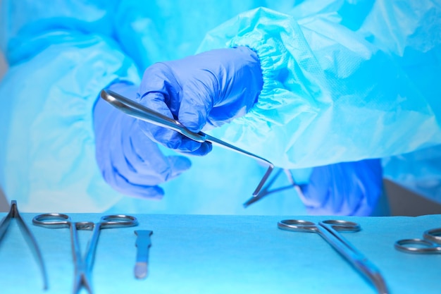 Close-up das mãos de cirurgiões no trabalho na sala de cirurgia em tons de azul. equipe médica realizando operação