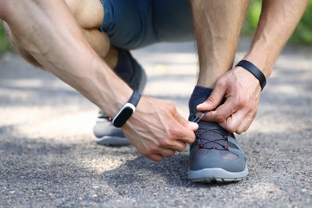 Close-up das mãos de pessoa do sexo masculino desportivo amarrando o cadarço. Tênis cinza elegantes para correr. Homem pronto para a corrida matinal. Rua da cidade. Treino e treinamento para um conceito de corpo forte