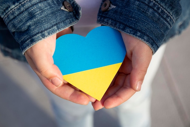 Close-up das mãos de uma criança segurando um coração nas cores da bandeira ucraniana mostrando apoio e solidariedade Protesto contra a invasão russa