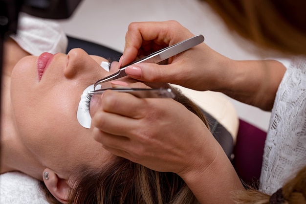 Foto close-up das mãos de uma esteticista aplicando cílios estendidos ao modelo.