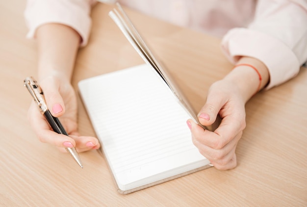 Close-up das mãos de uma mulher escrevendo em um bloco de notas colocado em um escritório doméstico de mesa de madeira e planos de conceito de trabalho e pensamentos