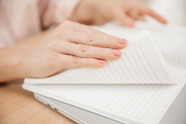 Close-up das mãos de uma mulher escrevendo em um bloco de notas colocado em um escritório doméstico de mesa de madeira e planos de conceito de trabalho e pensamentos