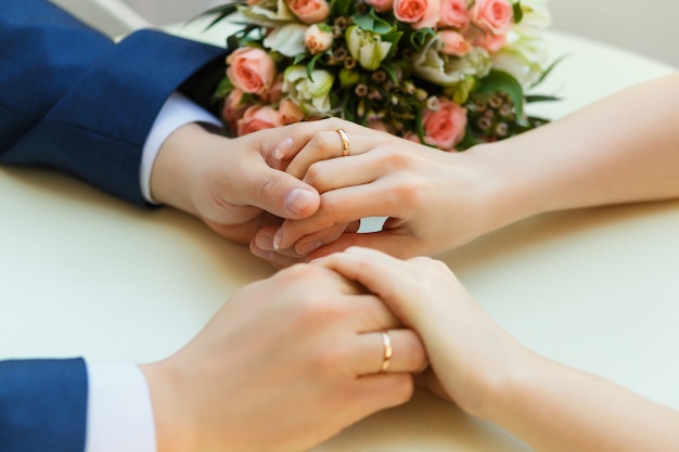 Close-up das mãos do casamento com anéis e buquê deitado na mesa