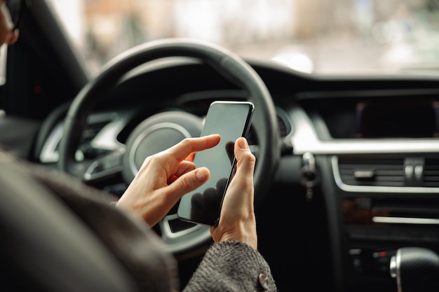 Close-up das mãos do motorista feminino está usando o telefone enquanto está sentado atrás do volante no próprio carro