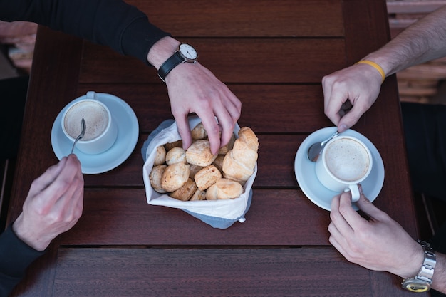 Close-up das mãos masculinas, bebendo café com biscoitos de queijo.