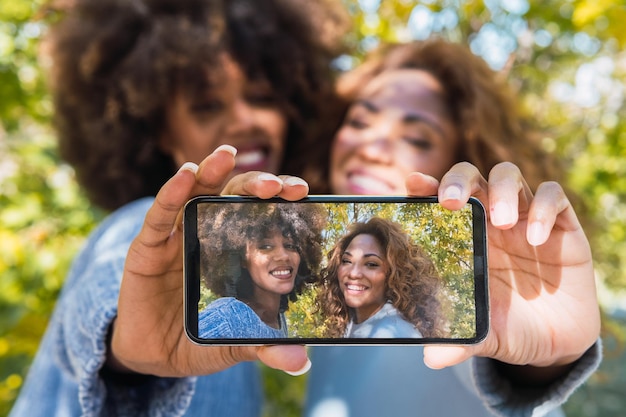 Close-up de amigos afro-negros em um humor divertido tirando selfie com smartphone usando a câmera frontal