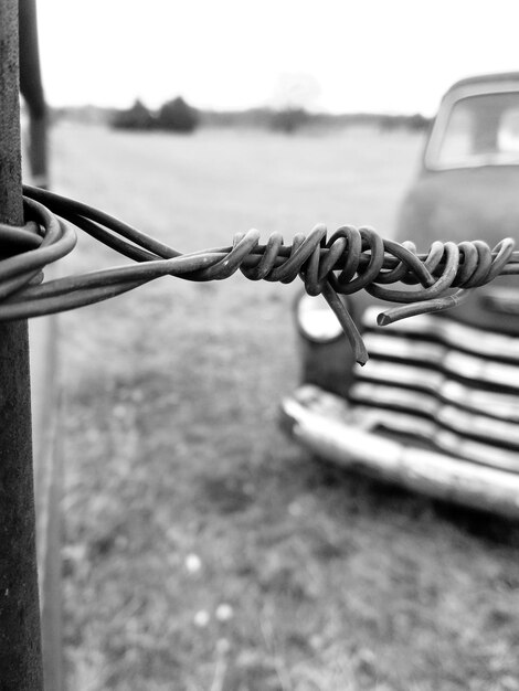 Foto close-up de arame farpado com carro vintage no fundo