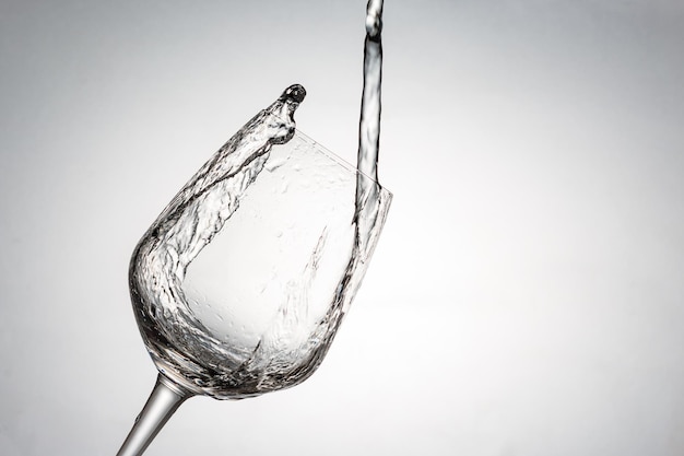 Close-up de bebida derramando em copo de vinho inclinado contra fundo branco