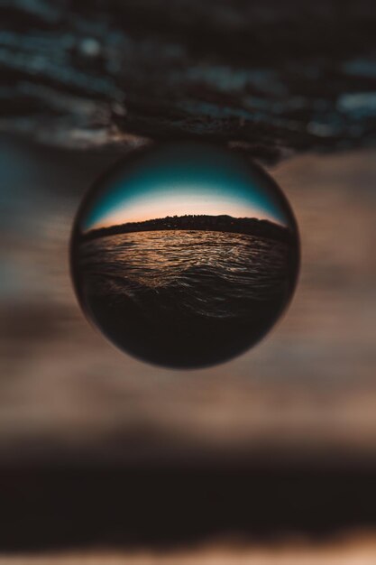 Foto close-up de bola de cristal com reflexo na água contra o céu no pôr do sol