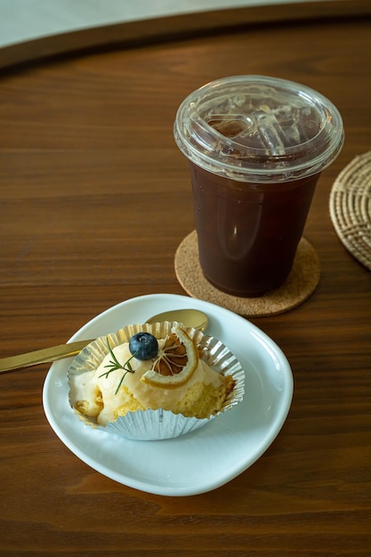 Close-up de bolo de laranja branco caseiro e café gelado Americano ou café preto na mesa de escritório de mesa de madeira na cafeteria no café no jardim durante o conceito de trabalho de negócios