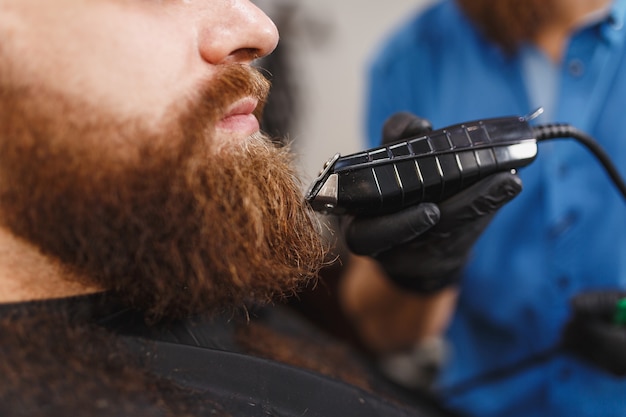 Close-up de cabeleireiro profissional atendendo cliente com barba espessa por tosquiadeira