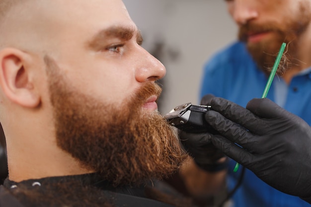 Close-up de cabeleireiro profissional atendendo cliente com barba espessa por tosquiadeira