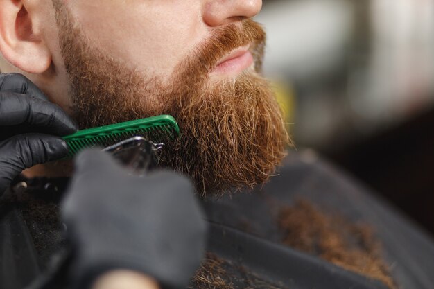 Close-up de cabeleireiro profissional atendendo cliente com barba espessa por tosquiadeira