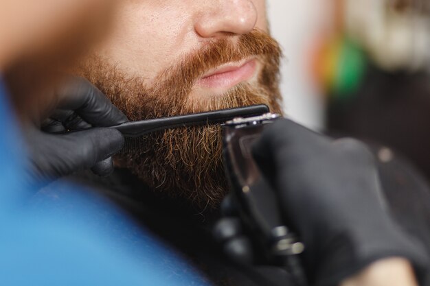 Close-up de cabeleireiro profissional atendendo cliente com barba espessa por tosquiadeira