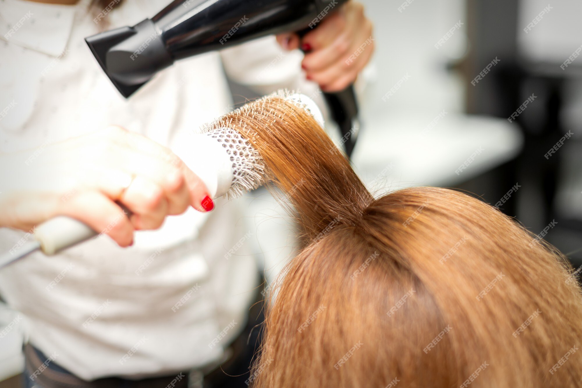 Secagem de cabelo no estúdio de cabeleireiro. estilista de cabeleireira  seca o cabelo com secador de cabelo e escova redonda ruiva de uma mulher em  um salão de beleza.