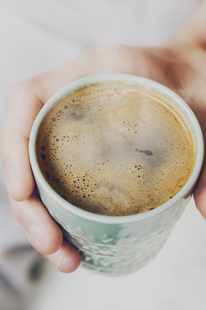 Close up de café expresso saboroso com espuma amarela saborosa em copo de cerâmica verde. Mãos masculinas segurando uma bebida quente quente. Toning.