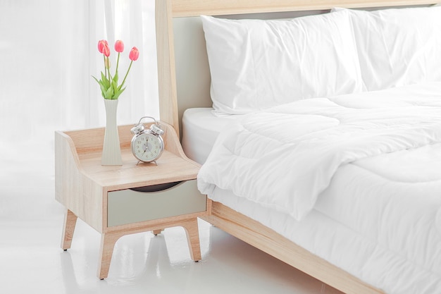 Close-up de cama moderna e armário de cabeceira com relógio e vaso de flores no quarto