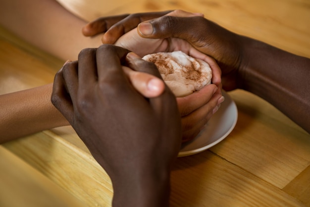 Foto close-up de casal de mãos dadas e xícara de café em uma cafeteria