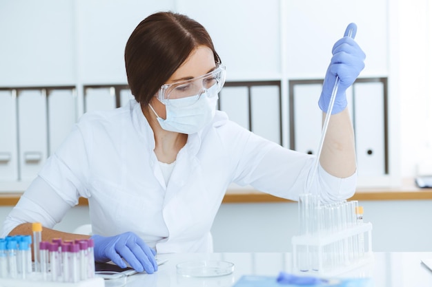 Close-up de cientista profissional feminina em óculos de proteção fazendo experimento com reagentes ou exame de sangue em laboratório. Conceito de medicina, biotecnologia e pesquisa.