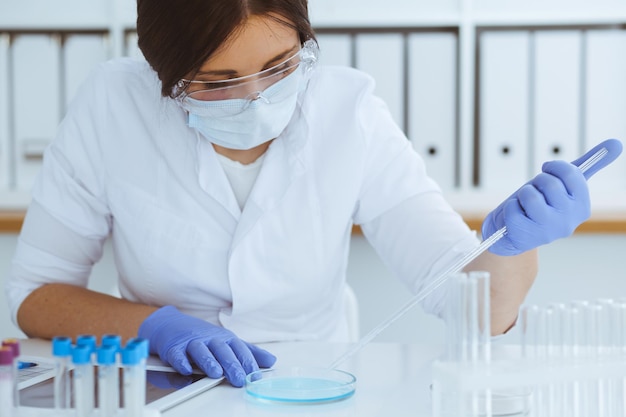 Close-up de cientista profissional feminina em óculos de proteção fazendo experimento com reagentes ou exame de sangue em laboratório. Conceito de medicina, biotecnologia e pesquisa.