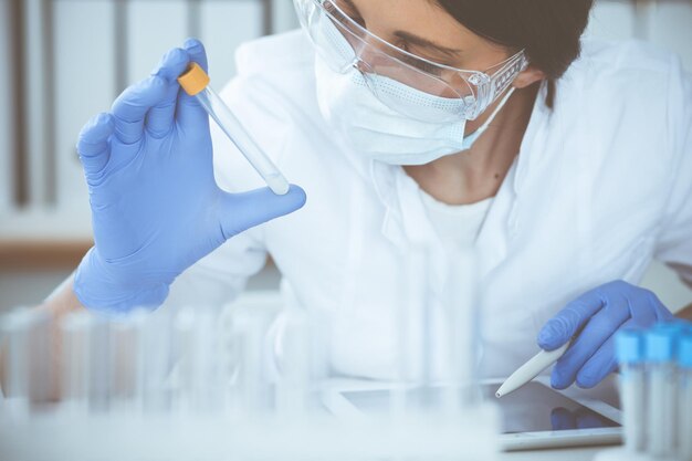 Close-up de cientista profissional feminina em óculos de proteção fazendo experimento com reagentes ou exame de sangue em laboratório. Conceito de medicina, biotecnologia e pesquisa.