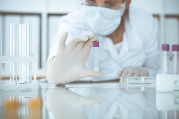 Close-up de cientista profissional feminina em óculos de proteção fazendo experimento com reagentes ou exame de sangue em laboratório. Conceito de medicina, biotecnologia e pesquisa.