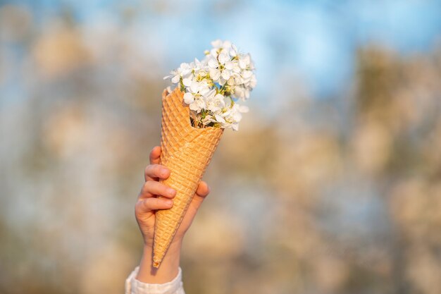 Close-up de cone de waffle cheio de flores de cerejeira, realizada por criança pequena contra