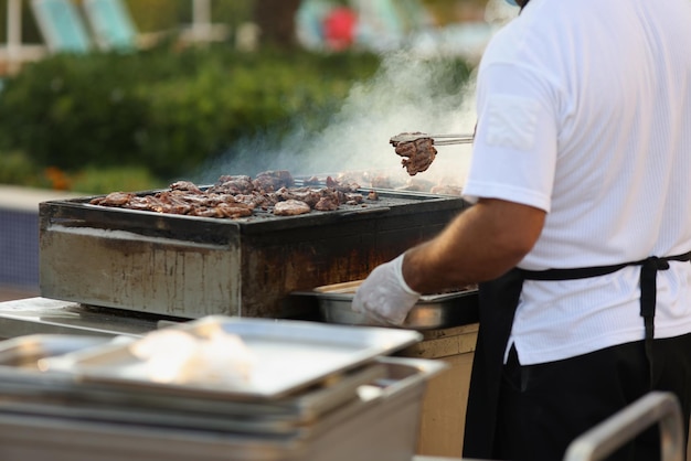 Close-up de construção metálica para fritar carne na natureza, chef masculino grelha. Piquenique ao ar livre, fritando carne e vegetais. Comida de rua, conceito de churrasco