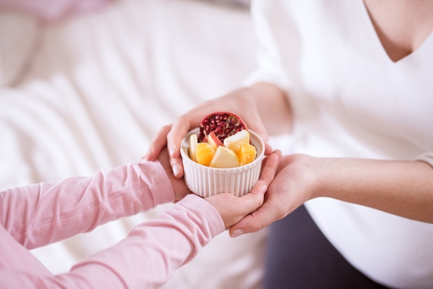 Close-up de cuidadosa menina criança traz salada de frutas para sua mãe.