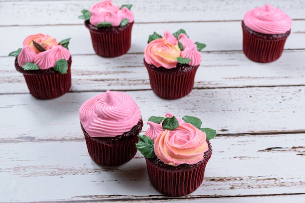 Close up de cupcake de veludo vermelho com cobertura de creme de manteiga rosa, rodeado por outros cupcakes.