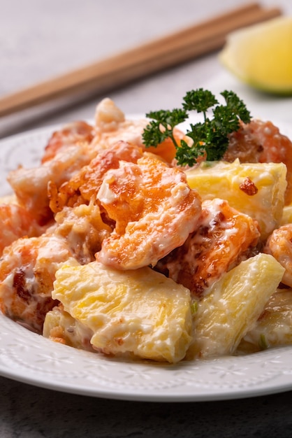 Close up de deliciosas bolinhas de camarão frito com molho de abacaxi e maionese em um prato branco na mesa cinza