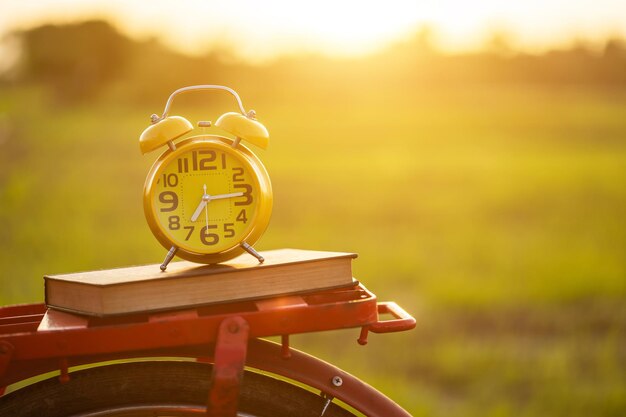 Foto close-up de despertador com livro em bicicleta ao pôr do sol