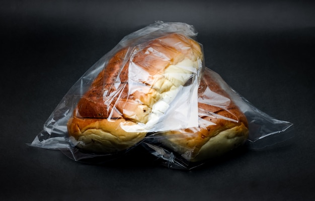 Close-up de dois deliciosos pães de trigo dentro de um saco plástico transparente em um fundo de textura escura