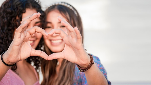 Foto close-up de duas garotas fazendo um coração moldar dois amigos juntos formando um sinal de mãos de amor de coração