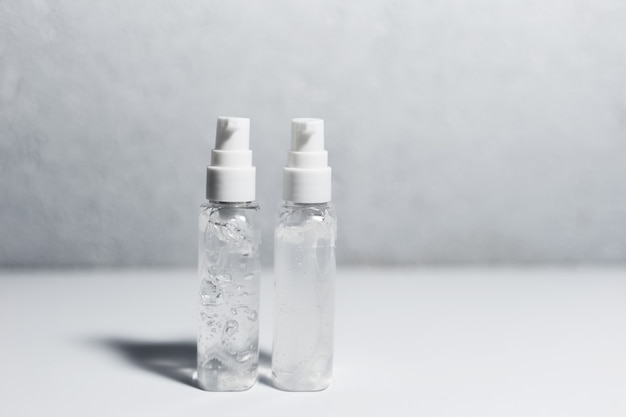 Close-up de duas garrafas plásticas portáteis com gel anti-séptico desinfetante na mesa branca. Superfície texturizada cinza.