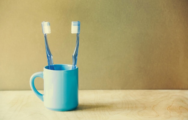 Foto close-up de escovas de dentes azuis em copo na mesa contra a parede