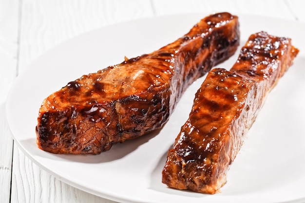 close-up de filé de salmão teriyaki em um prato branco sobre uma mesa de madeira texturizada