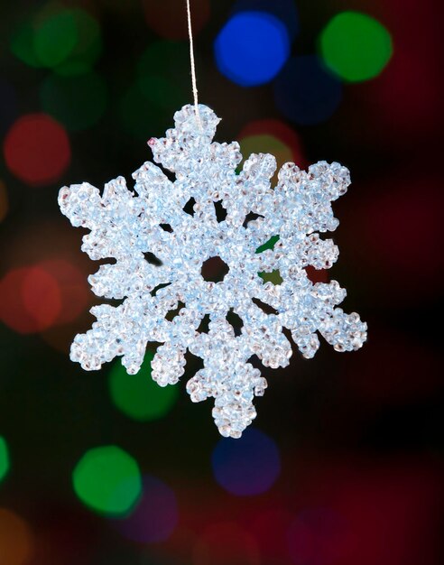 Foto close-up de floco de neve contra a árvore de natal iluminada