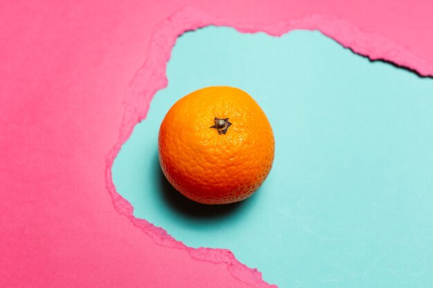 Close-up de fruta laranja em fundo ciano, em um buraco de papel rasgado de cor rosa.