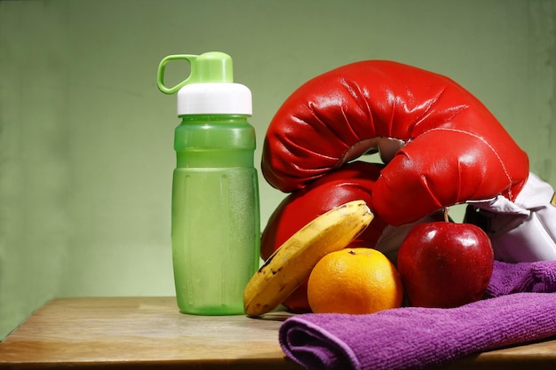 Close-up de frutas com luvas de boxe e garrafa de água na mesa contra fundo verde