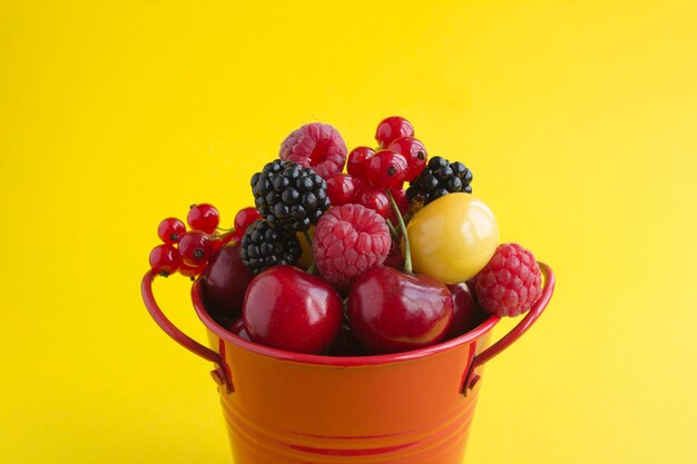 Close-up de frutas e bagas no balde vermelho sobre o fundo amarelo. Copie o espaço.